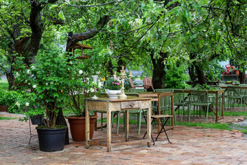Old wooden table and candlestick on the table. Tables and chairs in garden under the trees.