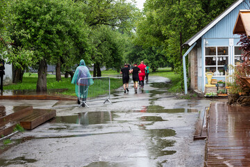 Athletes are running on the track during the rain in the park. Puddles on the track. A man in a raincoat is standing on track.