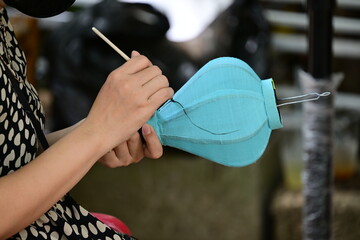 A young, Vietnamese girl starts painting a blue lampshade.