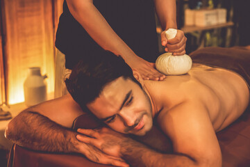 Hot herbal ball spa massage body treatment, masseur gently compresses herb bag on man body....