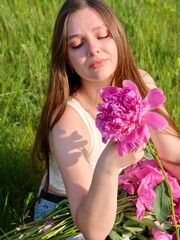 Happy smiling woman outdoors with pink peony flowers enjoying life in the moment at sunset