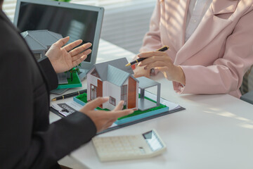 Inside a real estate office a real estate agent is using a house mockup to present the design and...
