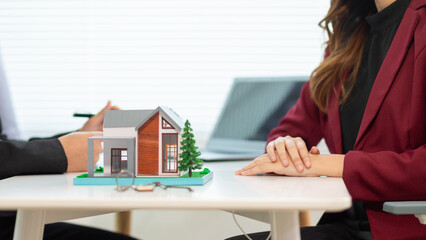 Inside a real estate office a real estate agent is using a house mockup to present the design and promotions that the client will receive when they sign sales contract. Real estate investment concept
