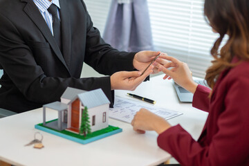 Real estate agent is talking to a customer inside office to hand over the house keys to the customer after the real estate sale contract is completed. Real estate investment concept