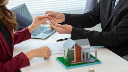 Real estate agent is talking to a customer inside office to hand over the house keys to the customer after the real estate sale contract is completed. Real estate investment concept