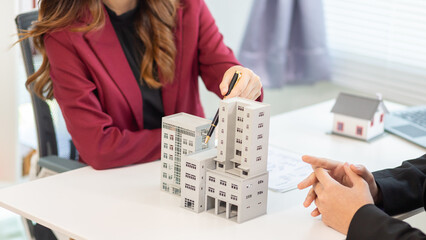 Inside a real estate office a real estate agent is presenting a condominium unit for sale to a client and offering a valuable promotion to entice the client to purchase their own property. copy space
