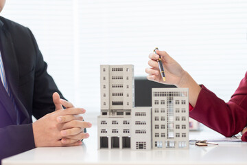 Inside a real estate office a real estate agent is presenting a condominium unit for sale to a client and offering a valuable promotion to entice the client to purchase their own property. copy space