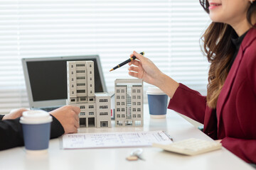 Inside a real estate office a real estate agent is presenting a condominium unit for sale to a client and offering a valuable promotion to entice the client to purchase their own property. copy space