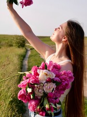 Happy smiling woman outdoors with pink peony flowers enjoying life in the moment at sunset