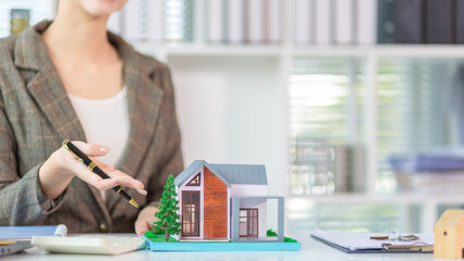 Inside a real estate office a real estate agent is using a house mockup to present the design and...