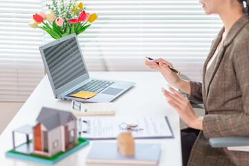 Inside a real estate office a real estate agent is using a house mockup to present the design and promotions that the client will receive when they sign sales contract. Real estate investment concept