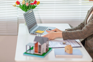 Inside a real estate office a real estate agent is using a house mockup to present the design and promotions that the client will receive when they sign sales contract. Real estate investment concept
