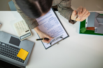 Real estate agent is in the office with the customer to prepare the documents for the real estate sale. The customer signs the sales contract before handing over the property to the customer.