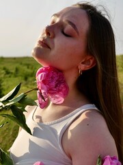 Happy smiling woman outdoors with pink peony flowers enjoying life in the moment at sunset