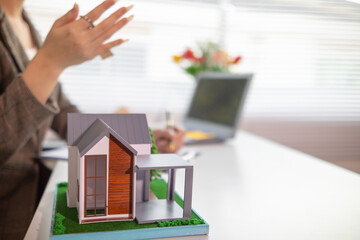 Inside a real estate office a real estate agent is using a house mockup to present the design and promotions that the client will receive when they sign sales contract. Real estate investment concept