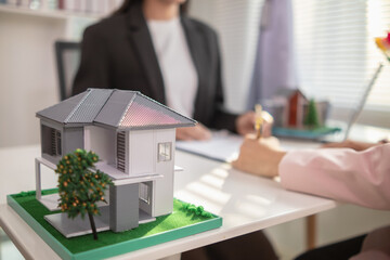 Inside a real estate office a real estate agent is using a house mockup to present the design and promotions that the client will receive when they sign sales contract. Real estate investment concept