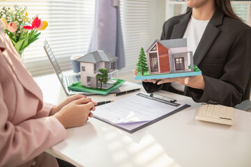 Inside a real estate office a real estate agent is using a house mockup to present the design and promotions that the client will receive when they sign sales contract. Real estate investment concept