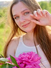 Happy smiling woman outdoors with pink peony flowers enjoying life in the moment at sunset