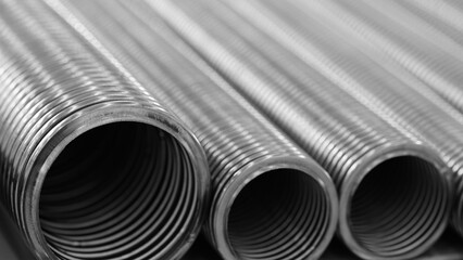 Row of stainless steel corrugated high pressure pipes in silver color. The pipes are long and thin. Mechanical industrial concept background