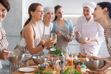 Young girl drinking glass of white wine and talking to other female cooking master class members whipping whites in bowls