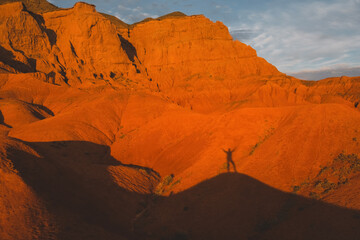 silhouette and shadow of tourist traveler against red desert mountains at sunset, Bogutty Ridge in spring Kazakhstan