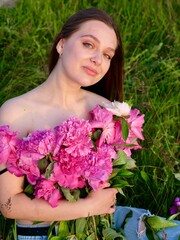 Happy smiling young woman in summer outdoors in a field with pink peony flowers enjoying life in a...
