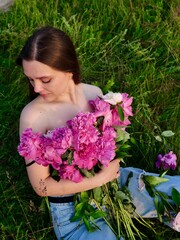 Fototapeta premium Happy smiling young woman in summer outdoors in a field with pink peony flowers enjoying life in a moment at sunset