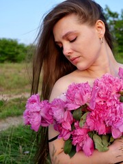 Happy smiling young woman in summer outdoors in a field with pink peony flowers enjoying life in a...