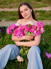 Happy smiling young woman in summer outdoors in a field with pink peony flowers enjoying life in a...
