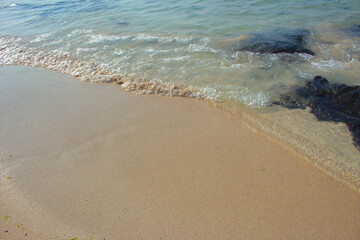 Beach sand with blue sea waves, and basalt rock