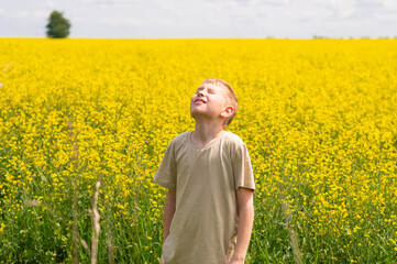 Fototapeta premium Blond boy enjoying a sunny summer day in a yellow rapeseed field