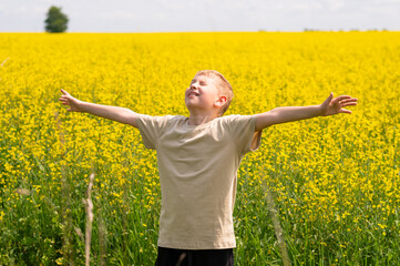 Happy blond boy with raised arms enjoying summer vacation in a yellow rapeseed field