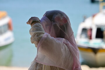An Arabian woman wears a white headscarf on the beach of an island in Vietnam while she is looking at her family.