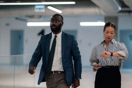 Businesspeople walking and checking time in office corridor - Powered by Adobe