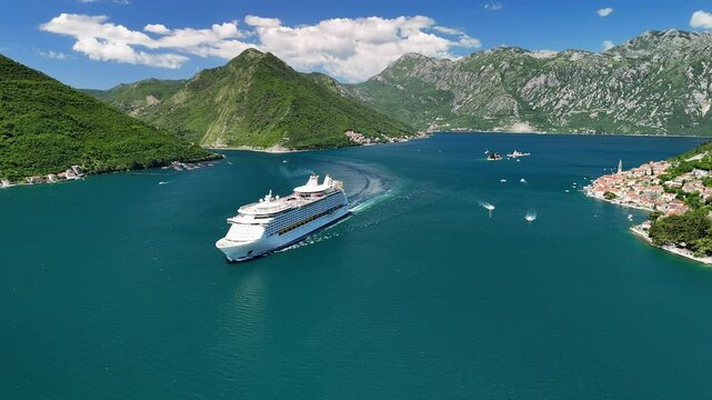 Aerial drone view of a cruise ship near the town of Perast, located in the Bay of Kotor. Tourist boats are sailing nearby. The island of Saint George is visible on the horizon. Montenegro, Europe.