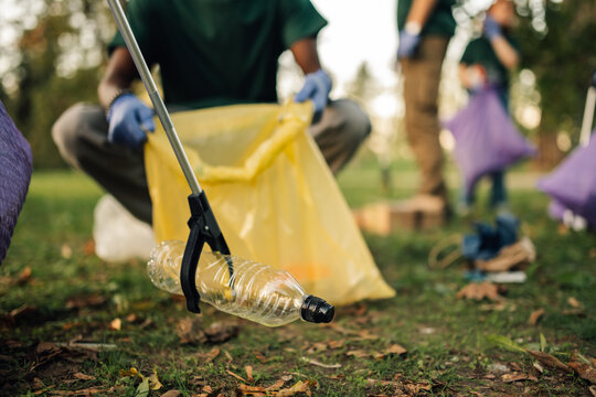 Volunteer picking up plastic bottle with trash grabber tool in park