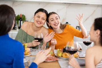 Girlfriends chatting and drinking wine at home party table in kitchen