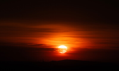 Fiery sunset over rolling hills serene twilight sky glowing orange and crimson sun silhouettes mountain ridge and wind turbines peaceful sustainable landscape inspiring nature photography reverie