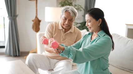 Fototapeta premium Happy elderly couple exercising together with dumbbells at home, focusing on muscle strength, joint health, and physical wellness for improved mobility and healthy aging. Retirement concept. Myrmidon.