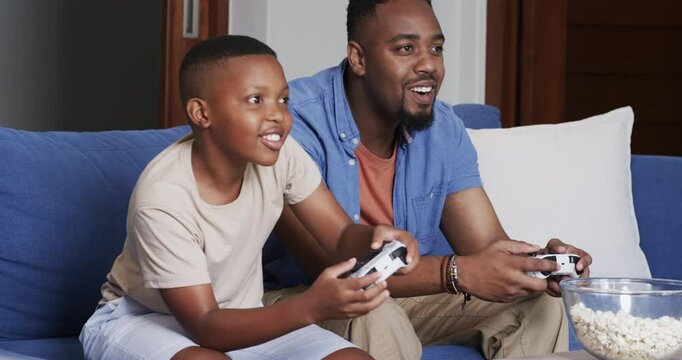 African American father and son tapping controllers on couch as game intensifying to win