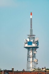 Tall communications and broadcast tower with satellite dishes on the rooftop