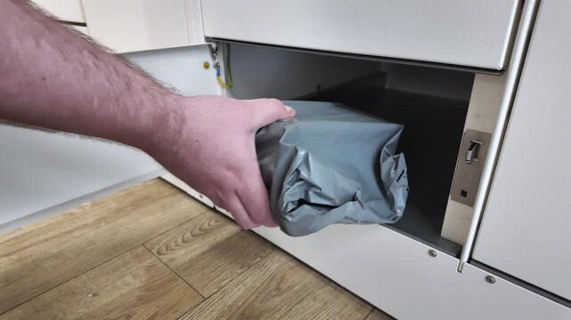 A person's hand inserting a gray package into an open automated parcel locker compartment, illustrating efficient self-service logistics for secure online order delivery and convenient pickup