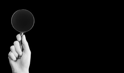 Hand holding magnifying glass in dark monochrome. Concept of secrecy, surveillance, censorship,