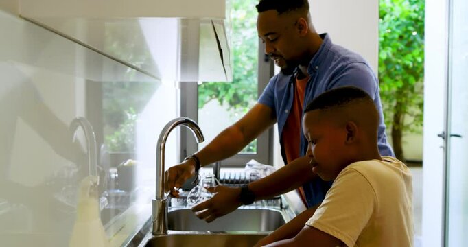 African American father and son washing dishes at kitchen sink father rinsing glass bonding