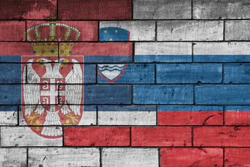 colourful painted big national flag of serbia and flag of slovenia on a massive old brick wall background. concept