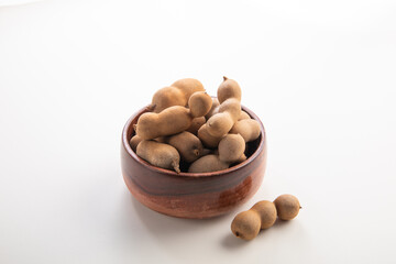 A bunch of Tamarind with shells in a wooden bowl on a white background