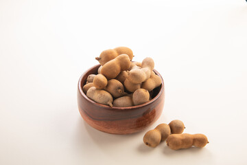 A bunch of Tamarind with shells in a wooden bowl on a white background