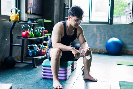 Young Asian man resting on training equipment in modern gym after workout session while preparing for next exercise
