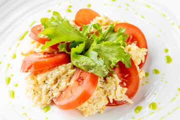 Fresh salad with scrambled eggs, sliced tomatoes, and green lettuce, garnished with green sauce on a white plate. A vibrant and healthy meal, ideal for food photography and culinary presentations.