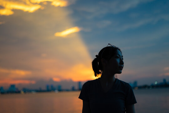 Sunset silhouette of a woman by the water in an urban environment during golden hour in the evening sky